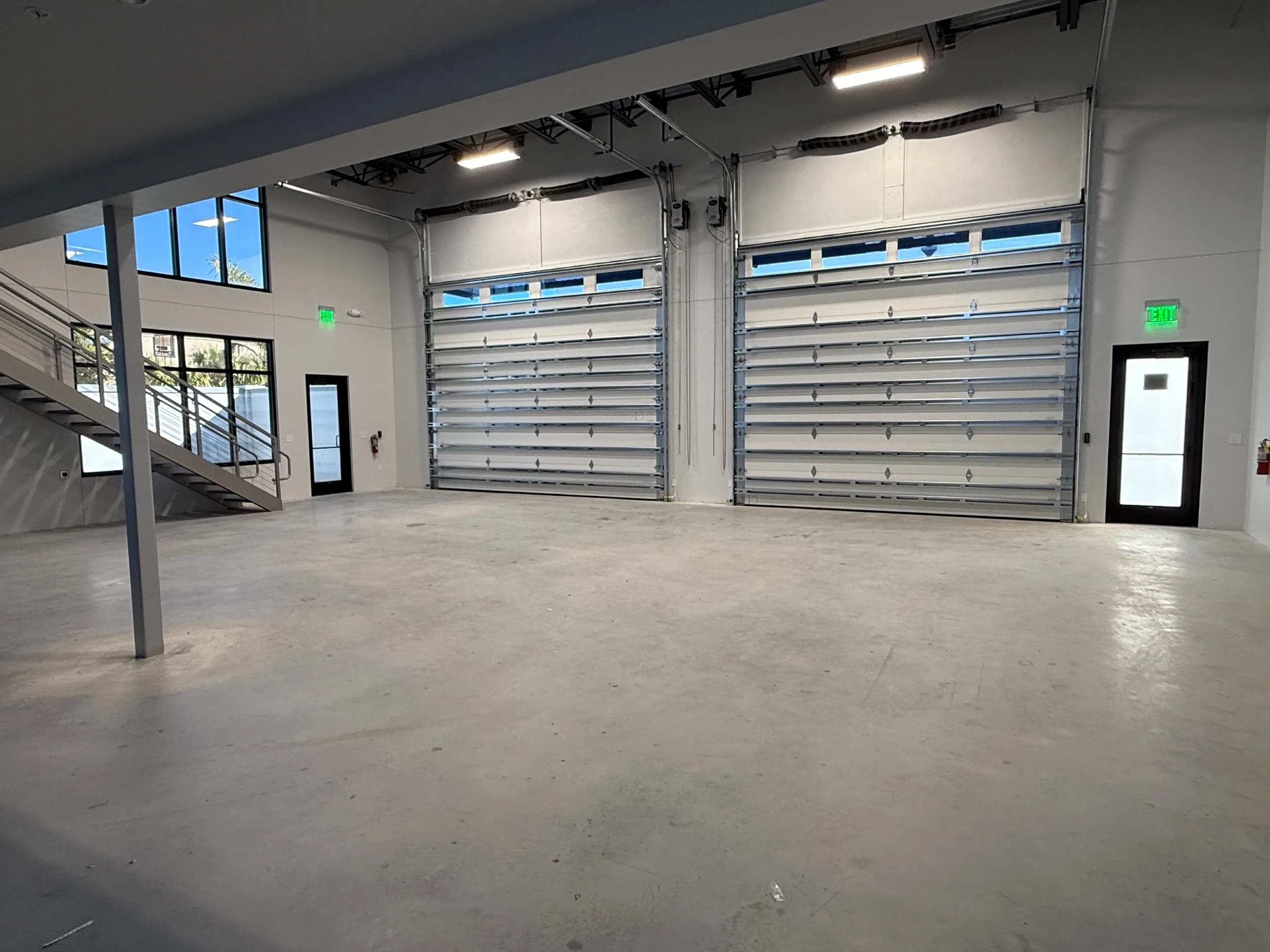 Drive-in motor coach storage unit with two aluminum roll-up doors, concrete floor, LED ceiling lights, and interior office/entry door