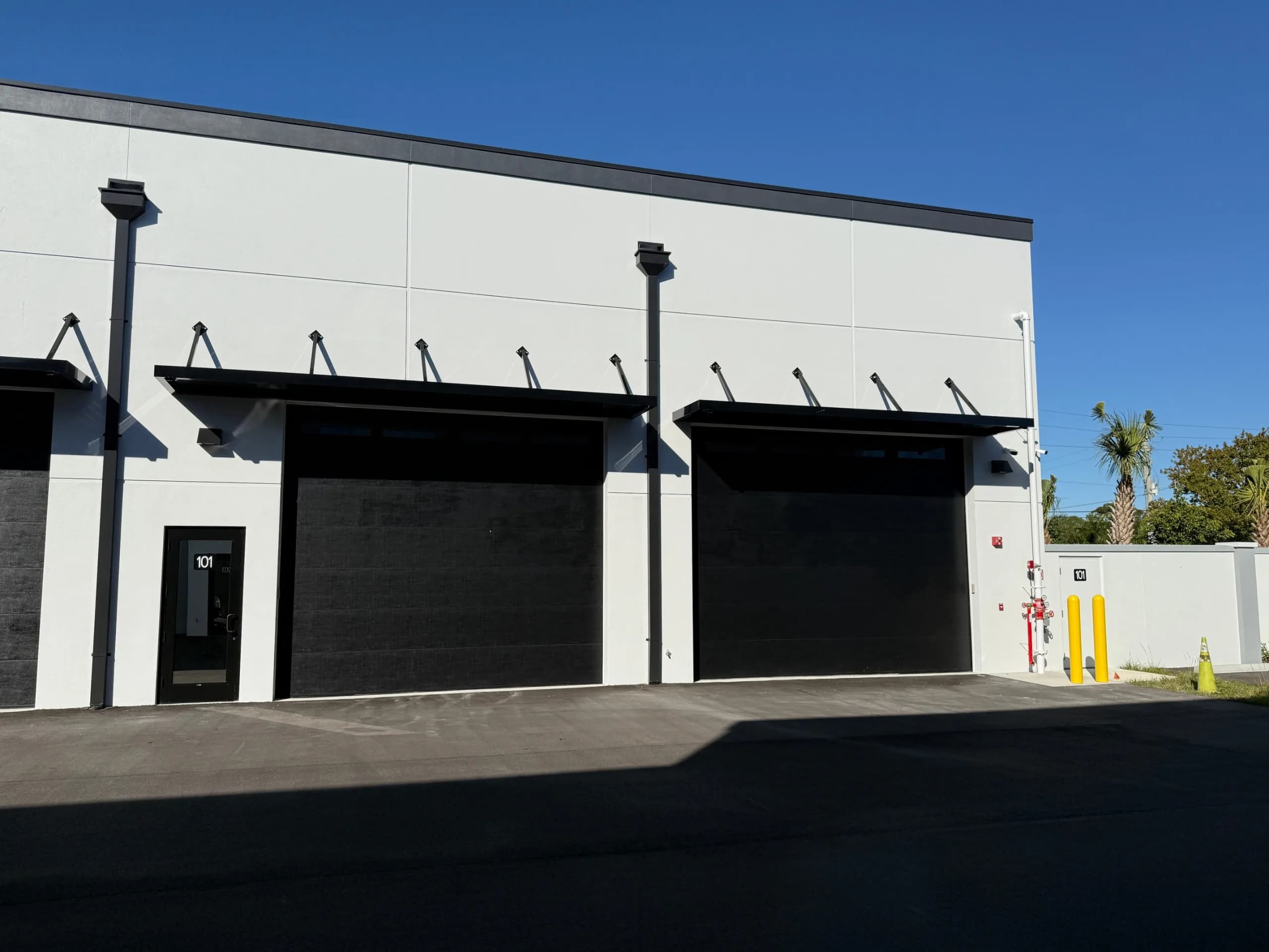 Two black roll-up garage doors on modern white building with metal awnings and numbered unit entrances