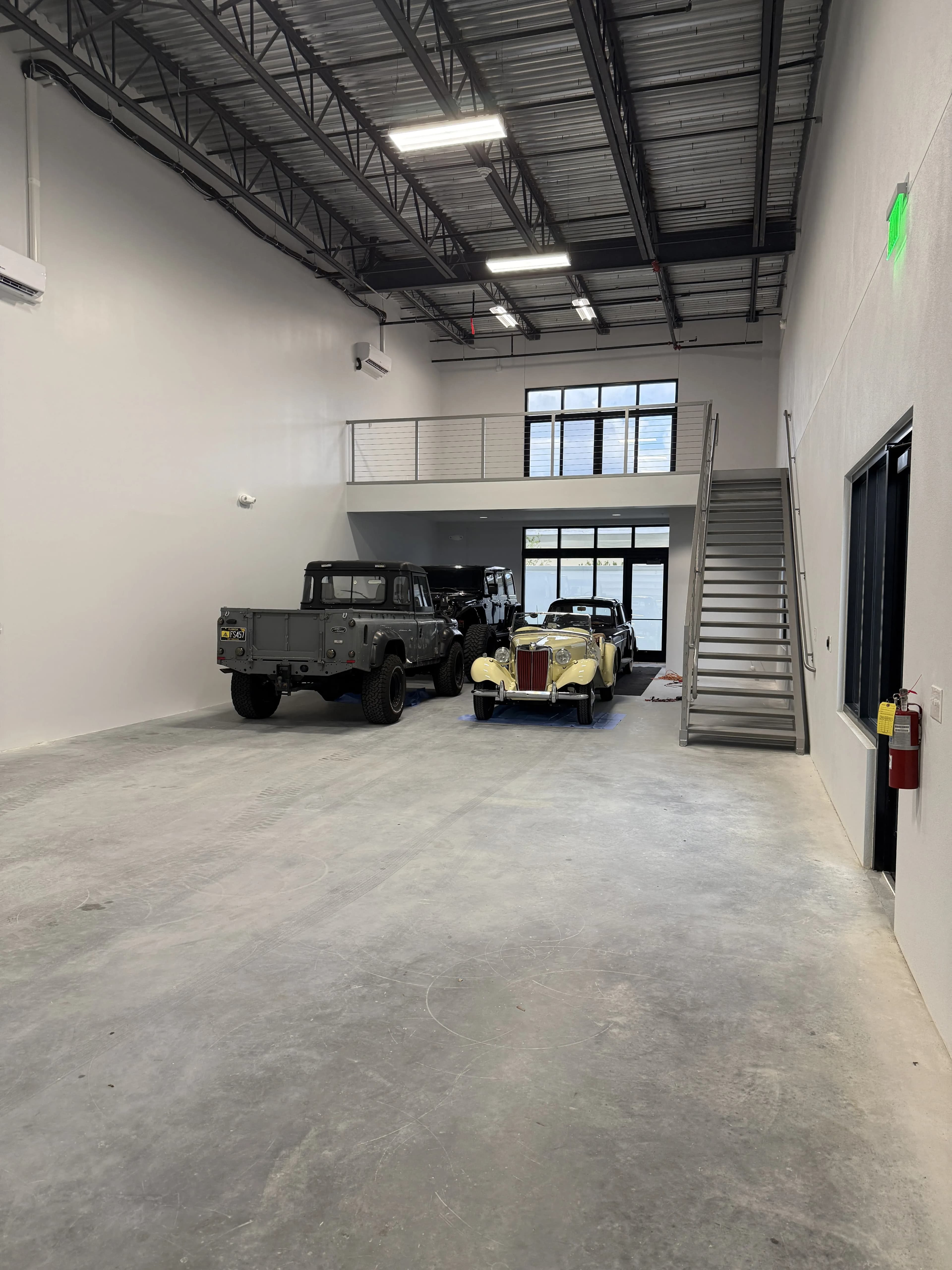 Garage floor with vintage Land Rover and MG, entry door and mezzanine above