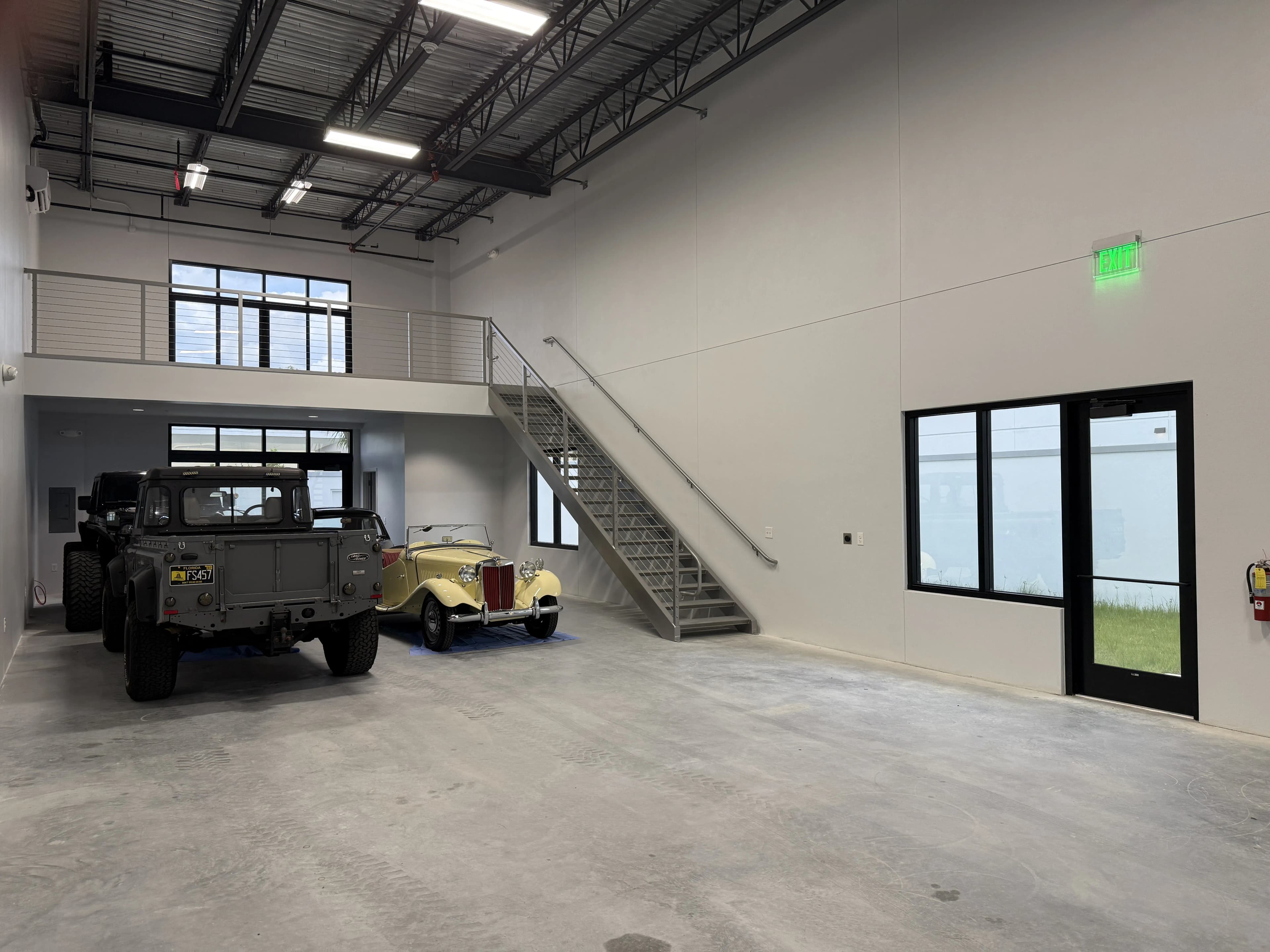 Wide view of garage floor with vintage vehicles, staircase, and glass entry door
