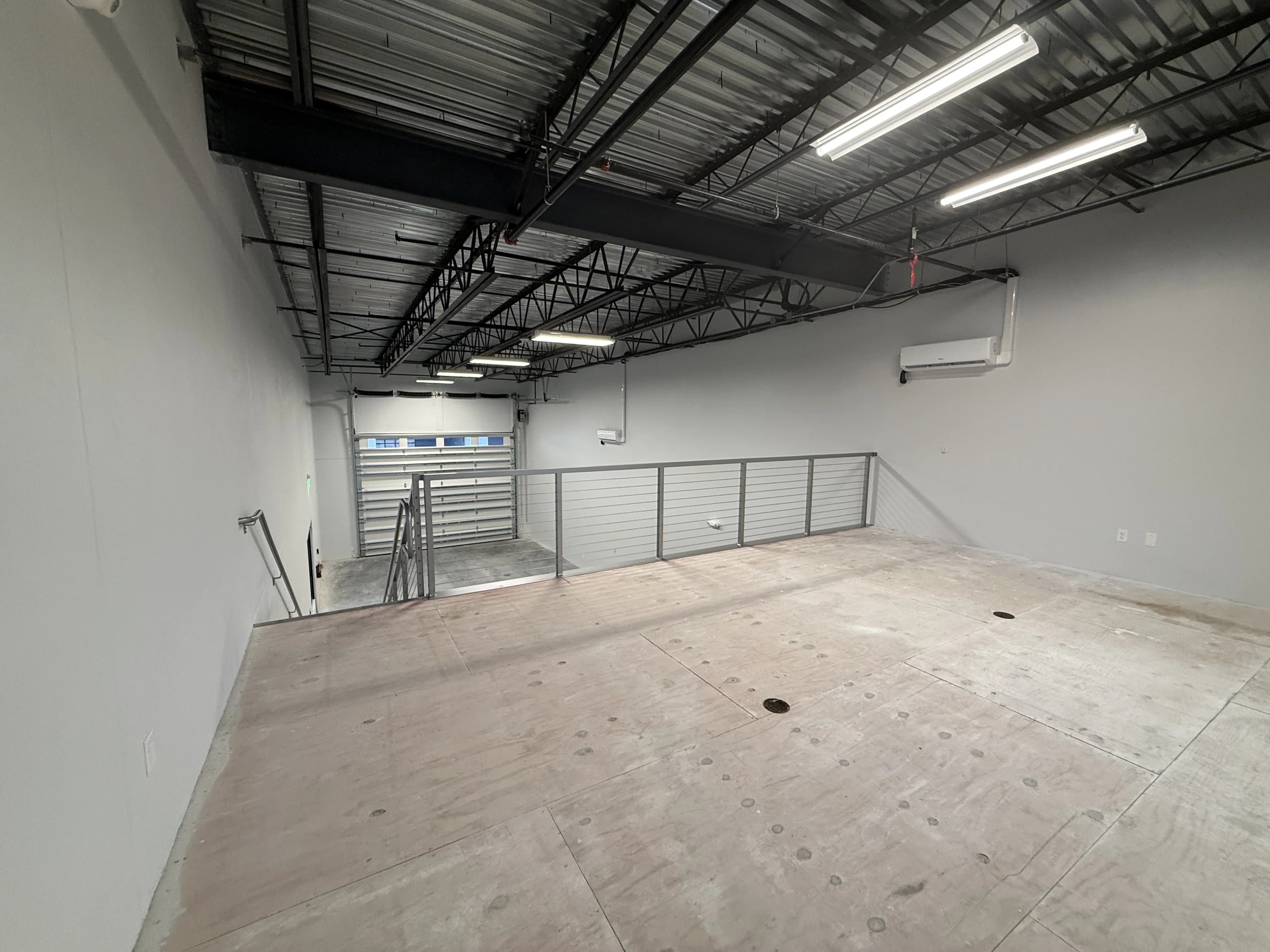 Mezzanine with plywood subfloor, garage door below, railing, and mini-split AC
